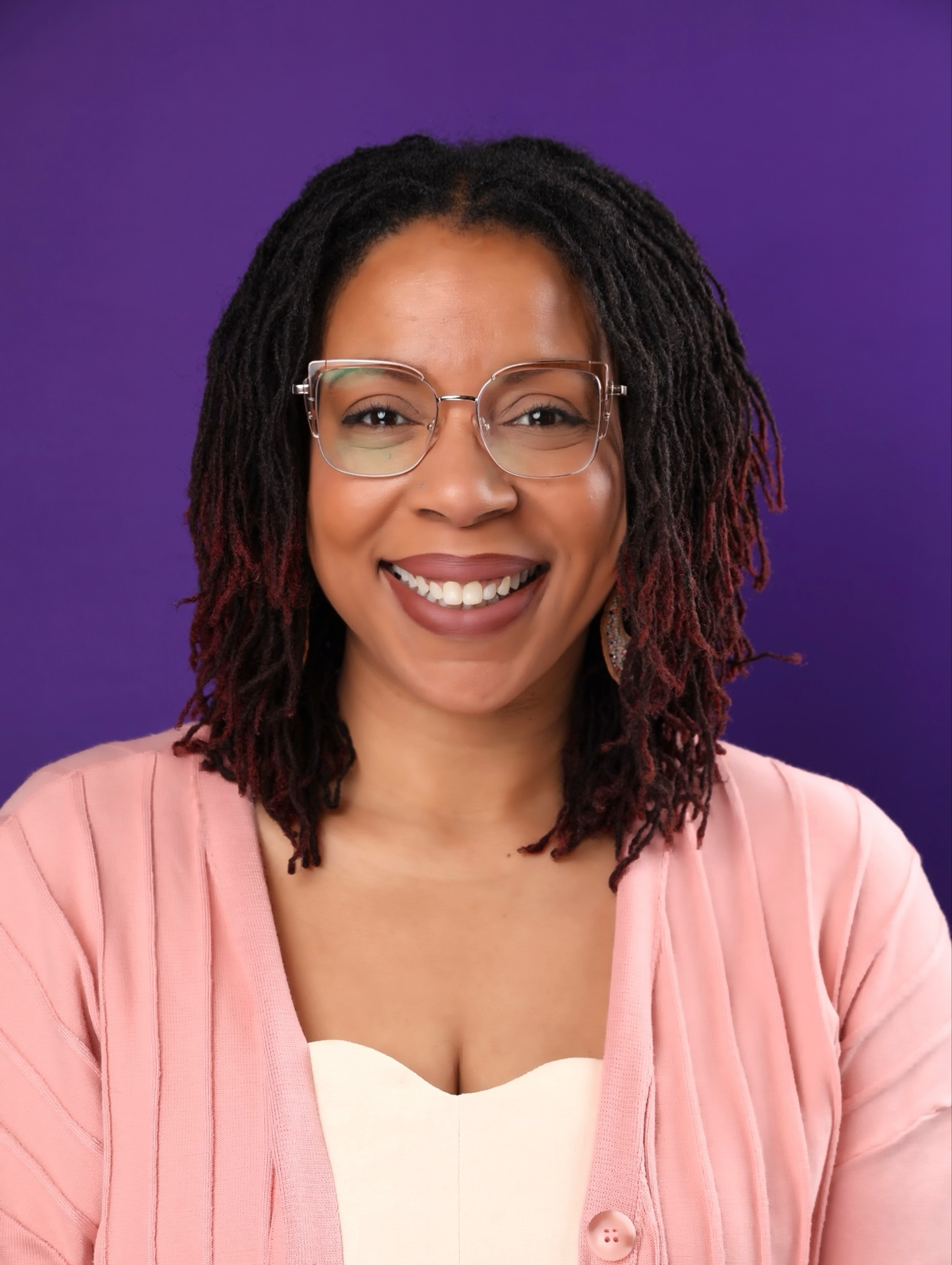 Lauran Peoples, smiling, in a pink cardigan against a purple backdrop.