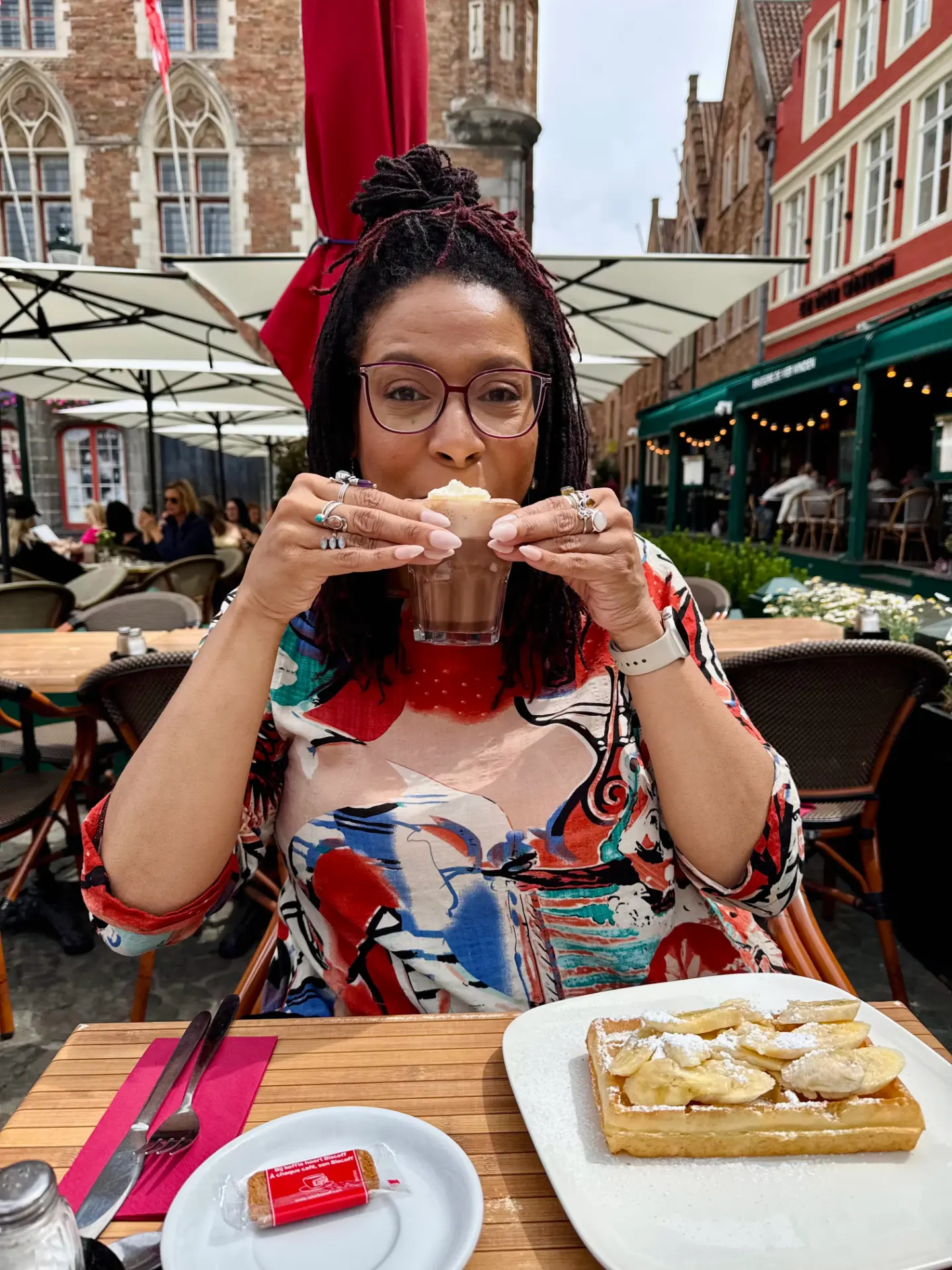 Lauran at an outdoor café table in Bruges, holding a hot chocolate.
